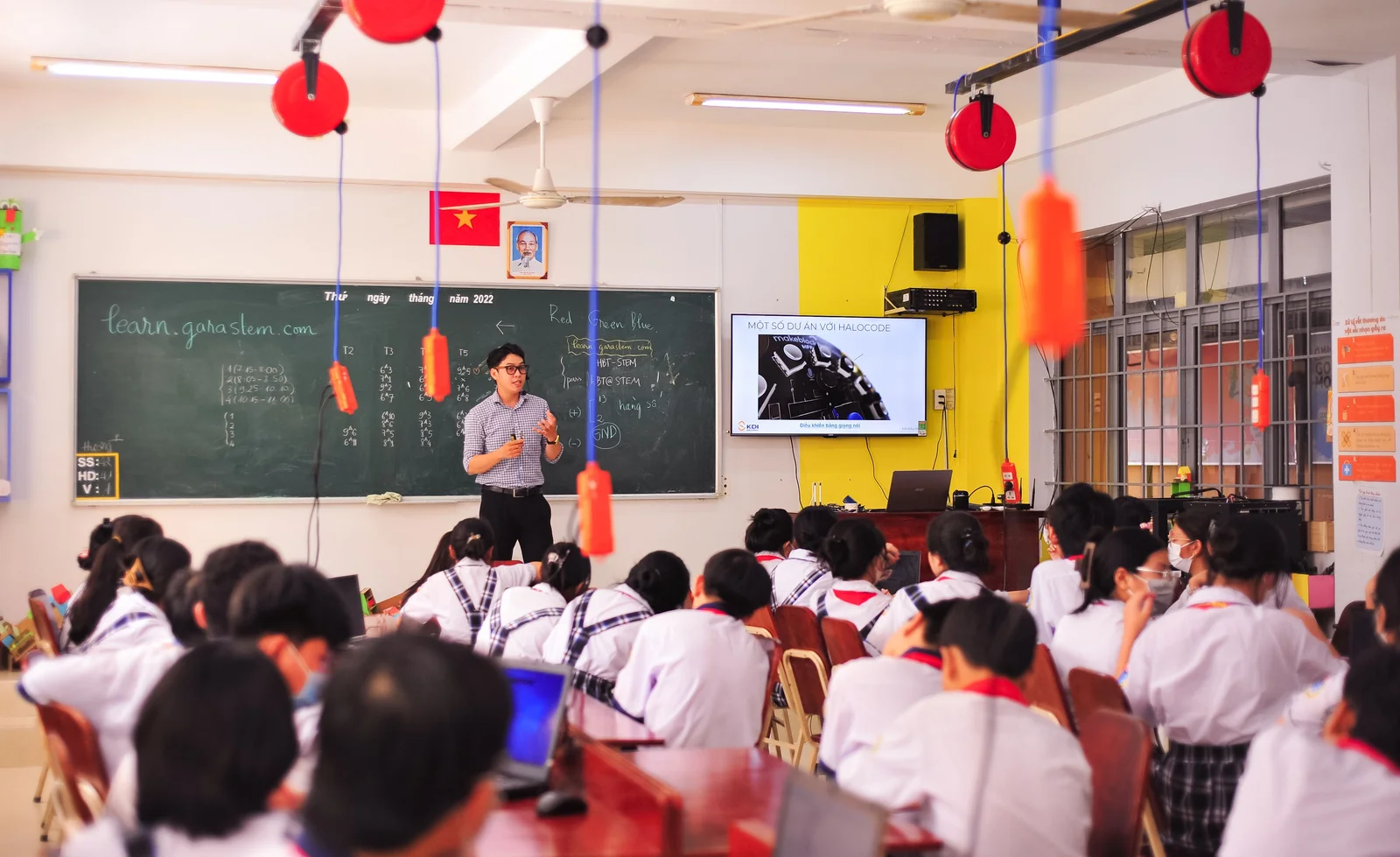 A teacher presenting to a classroom with a screen beside the chalkboard.