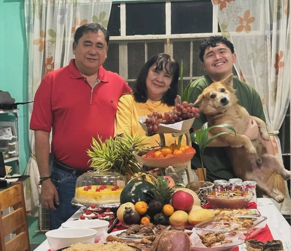 DJ with his parents and their dog around a table of food at home.