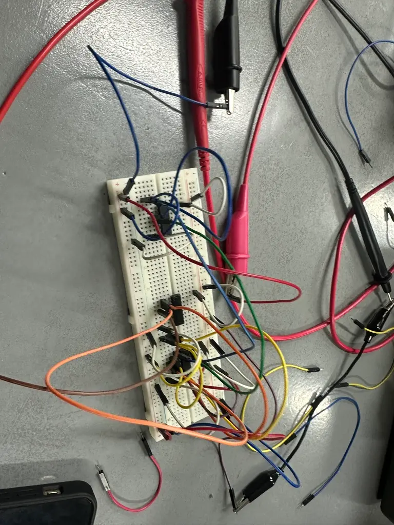 A breadboard covered in colorful jumper wires and logic chips, with multimeter probes clipped on.